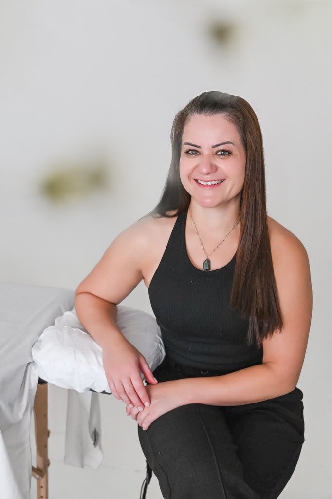 Grazi, massage therapist, smiling beside her treatment table