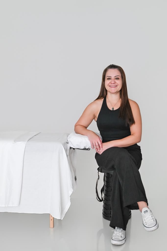 Grazi smiling beside her treatment table, ready for your session